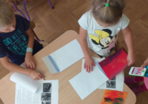Troje dzieci wkłada listy i rysunki do kopert.