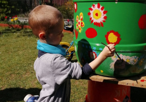 Chłopiec maluje farbami na plastikowej beczce.