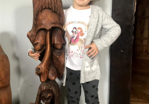 Dziewczynka stoi obok rzeźby z drewna.