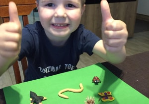 Uśmiechnięty chłopiec pokazuje kciuki w górę przy swojej pracy - zwierzątkach ulepionych z plasteliny.