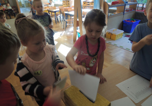 Dwie dziewczynki wrzucają kartkę do pudełka, oddając głos w wyborach do Rady Dziecięcej.