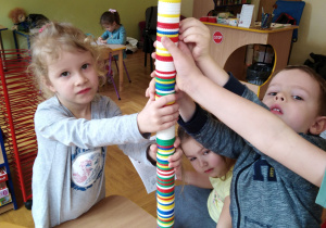 Troje dzieci trzyma wieżę ułożoną z guzików.