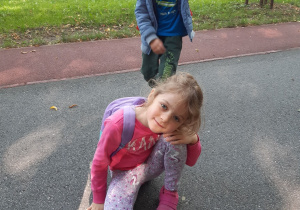 Dziewczynka kuca przy zrobionym z patyków i trawy gniazdku. Nad dziewczynką stoi chłopiec.