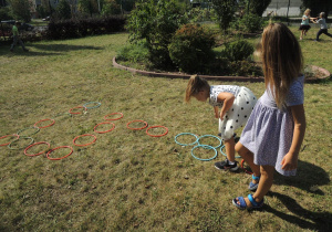 Dwie dziewczynki układają na trawie kolorowe obręcze.