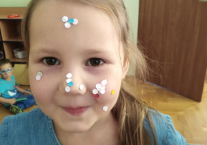 Dziewczynka ma na twarzy piegi zrobione z kółek z dziurkacza.