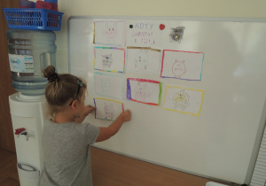 Dziewczynka przykleja rysunek kota na tablicy.