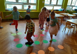 Dzieci skaczą po kolorowych kołach ułożonych w rzędy według kolorów.