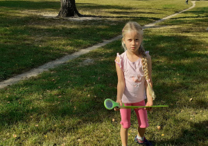 Dziewczynka z lupą i plastikową podkładką stoi na trawniku.