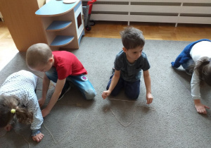 Dzieci układają na dywanie figury z włóczki.