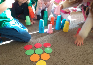 Dzieci układają wieżę z kolorowych kubeczków według instrukcji.