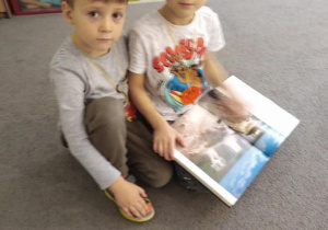 Dwóch chłopców na dywanie ogląda książkę.