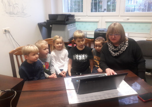 Pani Dyrektor i pięcioro dzieci siedzą przed laptopem.