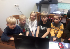 Czterech chłopców i dziewczynka siedzą przed laptopem.