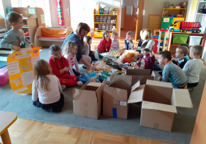 Dzieci na dywanie pakują karmę dla psów do kartonowych pudełek.