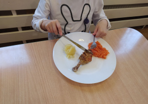 Dziecko je obiad posługując się nożem i widelcem.