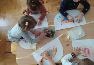 Dzieci rysują na papierowych fartuszkach.