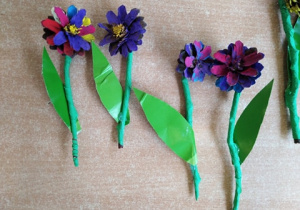 Kwiaty z pomalowanych szyszek na patyku owiniętym bibułą, z listkiem z zielonego papieru.