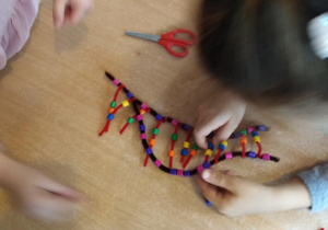 Dziewczynka robi model cząsteczki DNA, nawlekając koraliki na drucik kreatywny.