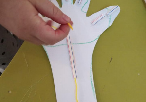 Dziecko przewleka nitkę przez słomki przyklejone do dłoni z papieru.