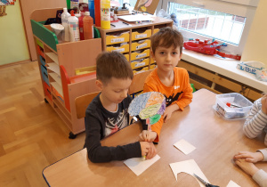 Dwóch chłopców mocuje papierowy model mózgu człowieka na patyku.