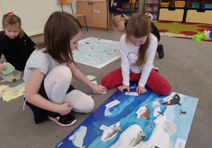 Dwie dziewczynki przyklejają opisy do plakatu przedstawiającego zwierzęta żyjące na Antarktydzie.