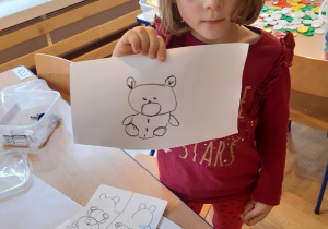Dziewczynka prezentuje misia narysowanego według instrukcji.