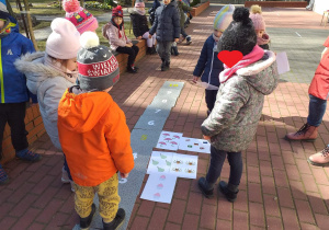 Na tarasie ułożona jest ścieżka z płytek z zapisanymi cyframi. Dzieci przyporządkowują kartki z różnymi obrazkami do liczby.