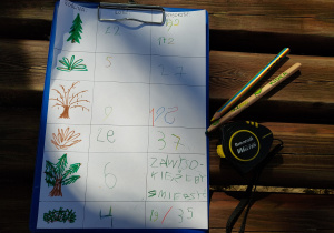 Karta pracy zawierająca rysunki drzew i krzewów, ich ilość i wysokość. Obok kartki leżą dwie kredki i miarka.