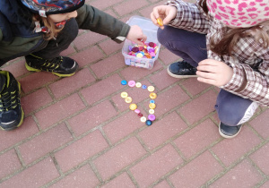 Dwoje dzieci układa trójkąt z guzików.