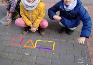 Dwie dziewczynki ułożyły z kolorowych patyków kwadrat, trójkąt i prostokąt.