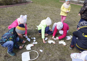 Dzieci układają papierowe pisanki przy sylwetach kur.