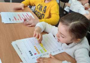 Dzieci przy stoliku kolorują w kartach pracy.
