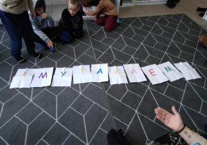Dzieci patrzą na kartki z literami ułożone na dywanie.