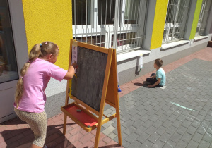 Dziewczynka sprawdza coś na tablicy stojącej na tarasie.