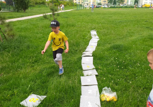 Chłopiec układa na trawie ścieżkę z ponumerowanych kolejno płytek.