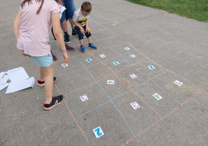 Dzieci rozwiązują sudoku liczbowe na kratownicy narysowanej kredą na asfalcie.