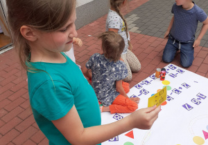 Dzieci grają na tarasie w samodzielnie zrobioną grę planszową.
