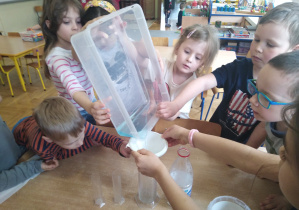 Dzieci przelewają wodę z plasikowego pojeminka do menzurki.