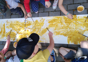 Dzieci malują kurkumą na długim arkuszu papieru.