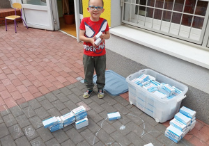 Chłopiec układa budowlę z kartonowych pudełek po lekach.