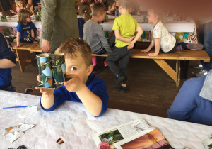 Dziecko, siedzące przy stole, trzyma swój organizer z rolek okleonych kawałkami gazet.