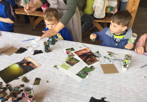 Dzieci przy stole okejają rolki po papierze kawałkami kolorowych gazet.