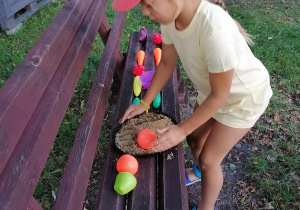 Dziewczynka układa plastikowe owoce na tarcie z piasku.