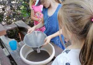 dziewczynka przesiewa piach do miski.