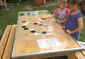 Dwie dziewczynki grają w grę planszową przy ławostole edukacyjnym w ogrodzie przedszkolnym.