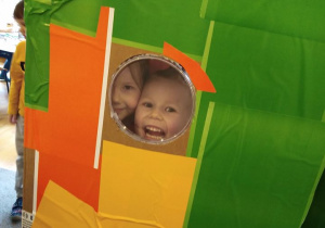 Dwoje uśmiechniętych dzieci spogląda przez okrągłe okienko.