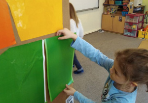 Dziewczynka ozdabia kartonową rakietę zielonym papierem samoprzylepnym.