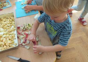 Dziecko zbiera ze stolika skórki jabłka.