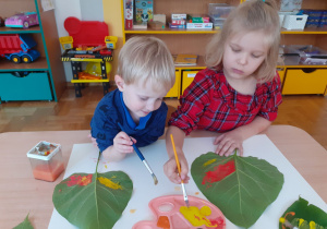 Dzieci malują liście kolorowymi farbami.