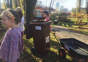 Dziewczynka ciągnie wózek obok kontenera na bio odpady.